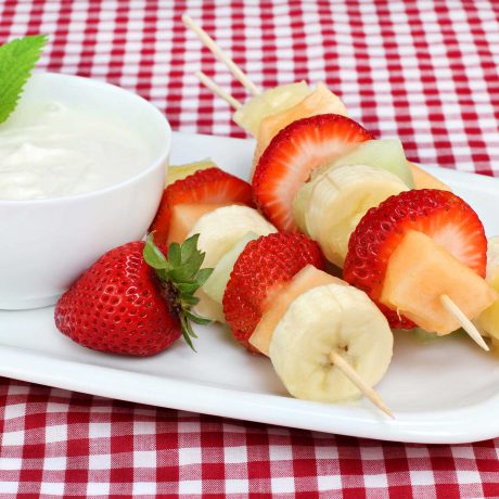 brochettes de fruits sur une assiette blanche près d'un bol de yogourt